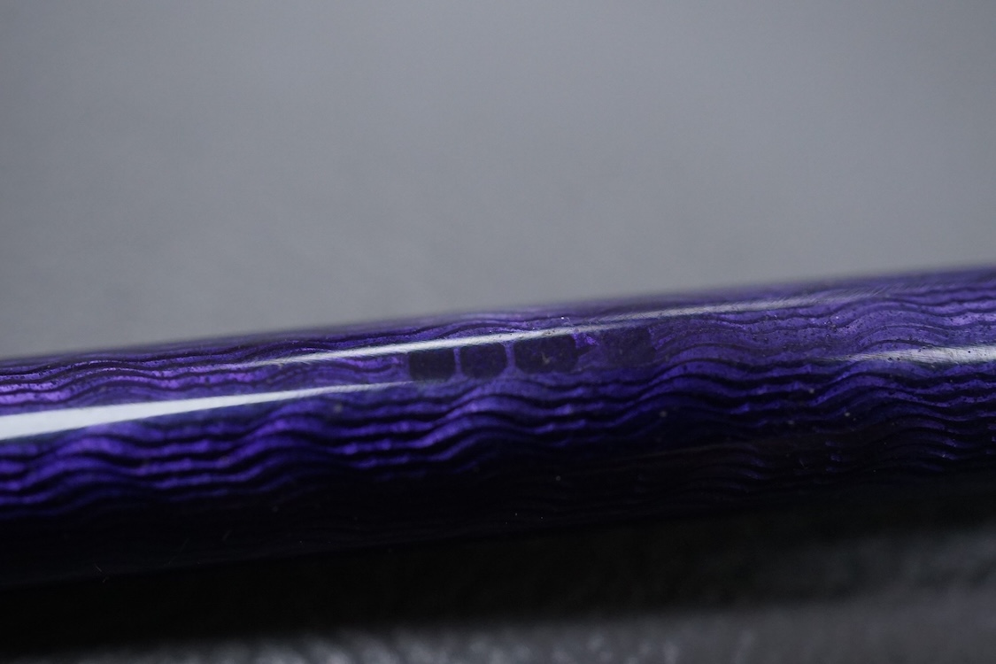 A silver and purple guilloche enamel pen, with ringed black enamel and globe terminals, one unscrews to reveal the pen tip, hallmarks beneath the enamel, possibly London, 1979, 13.9cm.